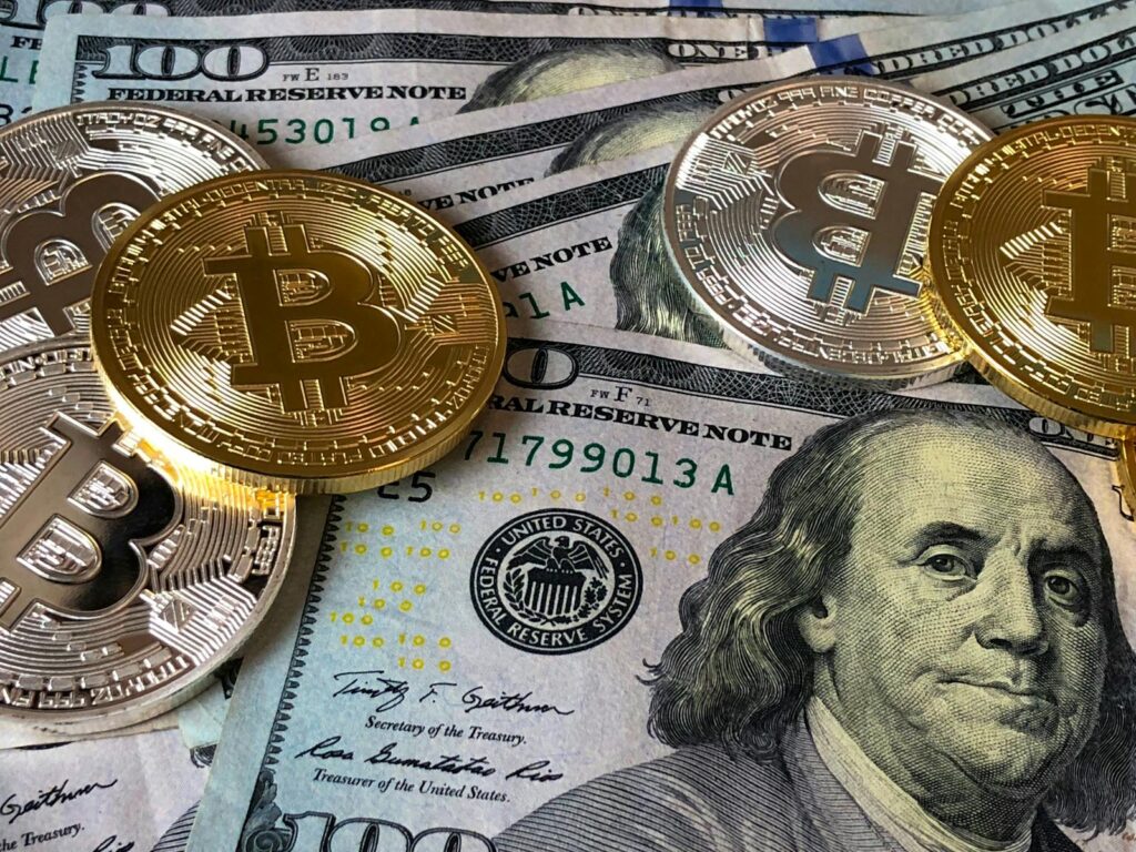 A close-up photo depicting Bitcoin coins on top of US dollar symbolizing physical and cryptocurrency.